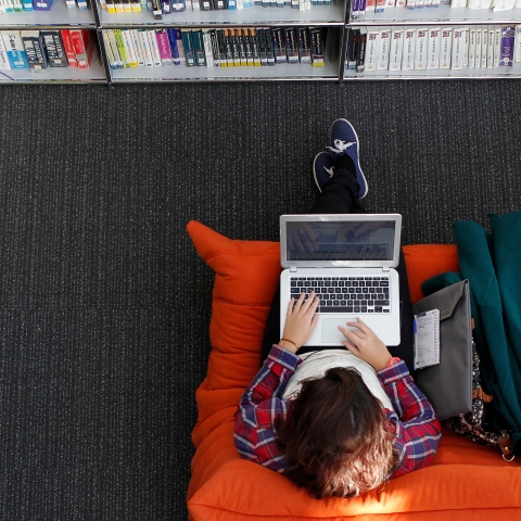 Aerial view of a person sitting on an orange sofa using a laptop