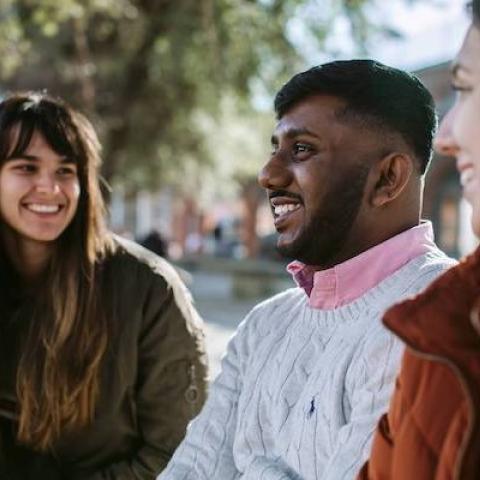 3 students sitting under a tree talking and smiling