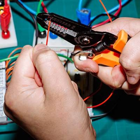 Close up of hands using wire cutters to cut an electrical cable