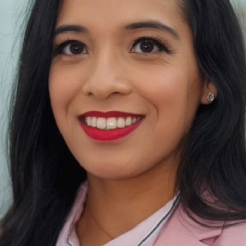 Ahsana smiling to camera wearing red lipstick, pink blazer and white shirt