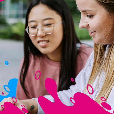 Two students are looking at a laptop screen together, displaying interest and collaboration in their task.