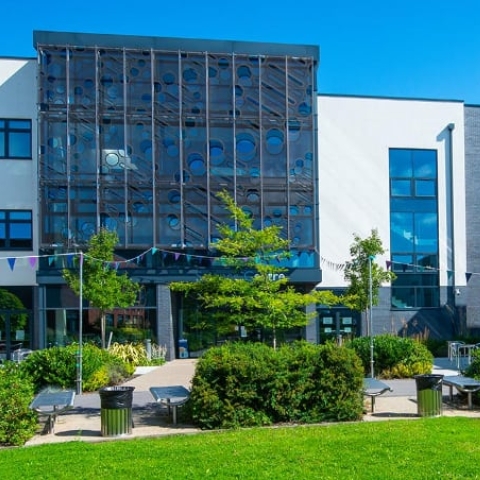 A modern building with trees and bushes around it, part of Barton Peveril Sixth Form College Campus