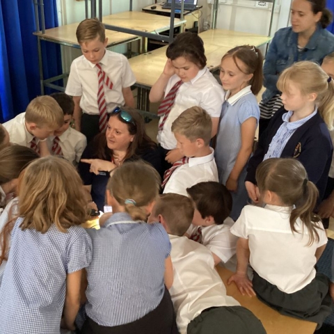 Dr Fay Couceiro looking through a microscope surrounded by children