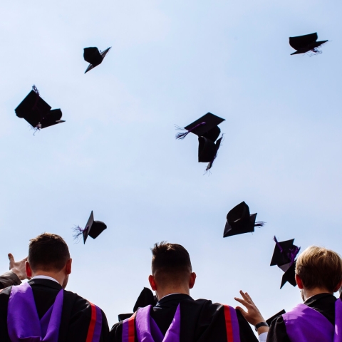 Shot from behind of graduates throwing their graduation caps up in the air