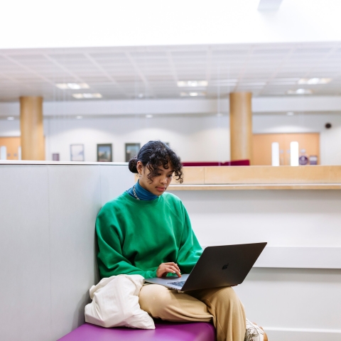 girl in green sweatshirt sitting with a laptop on a bench