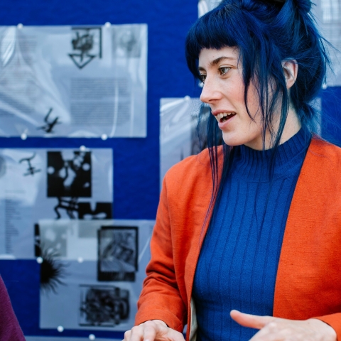 A person talking whilst stood in front of a poster board