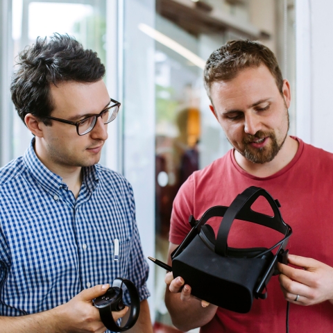 A staff member explaining to another staff member how a VR headset works