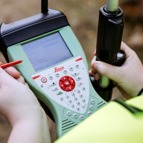 Student kneels next to the drone taking readings on touchpad outside Technology Facilities