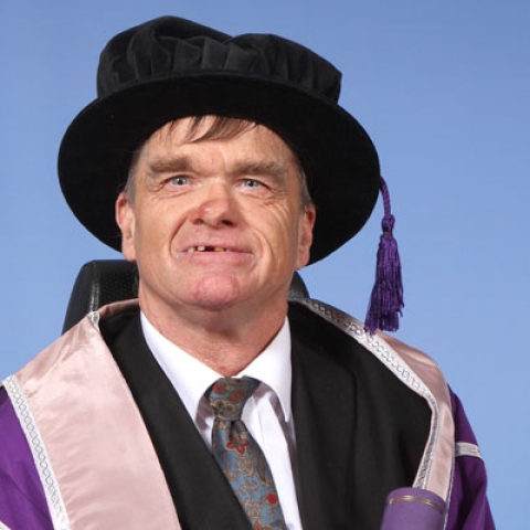 Kevin Holmes holding scroll in graduation gown and cap smiling to camera