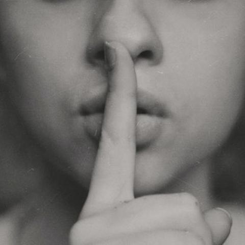 A close up photo of a person with their index finger to their lips