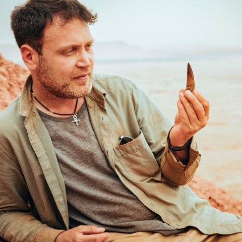 Dr Nizar Ibrahim in the Sahara desert holding a dinosaur tooth