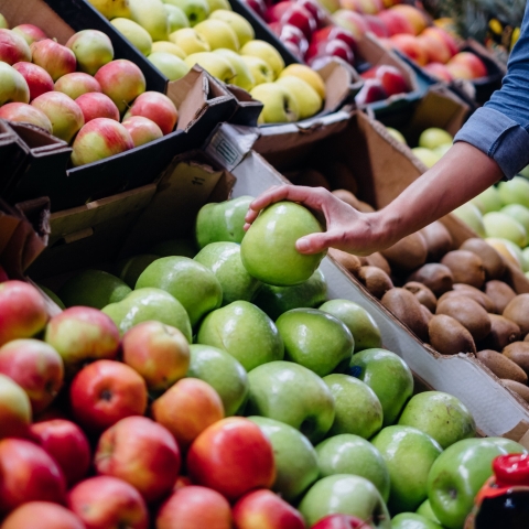 Woman's hand picks up a green apple from a crate of green apples
