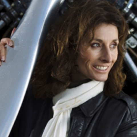 Tracey Curtis Taylor in leather jacket and scarf leaning against plane
