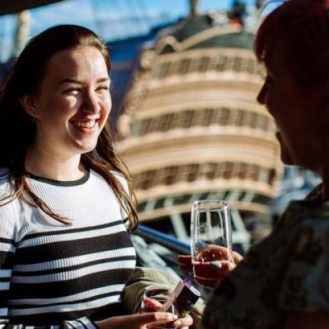 2 women talking in the sunshine with HMS Victory behind them.