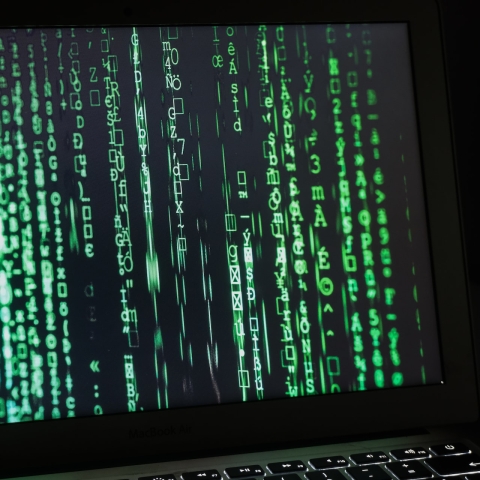 A close-up of a computer screen in a dark room with lots of green numbers, letters and symbols on a black background