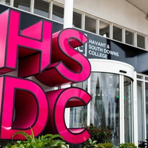 A bight pink sculptural interpretation of the Havant and Southdowns College logo outside the entrance to a modern college building 