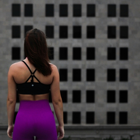 woman with her back to camera, wearing sports bra and purple leggings