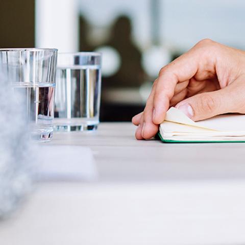 Close up of arm resting on table with notebook and pen