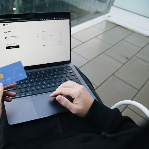 Image shows someone using a laptop and holding a debit or credit card as if purchasing an online product or service