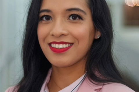 Ahsana smiling to camera wearing red lipstick, pink blazer and white shirt