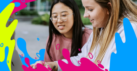 Two students are looking at a laptop screen together, displaying interest and collaboration in their task.