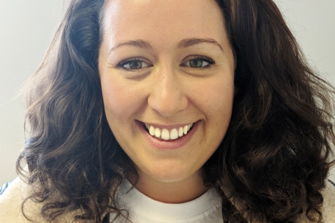 Becca Dean smiling to camera wearing aviator jacket and white top