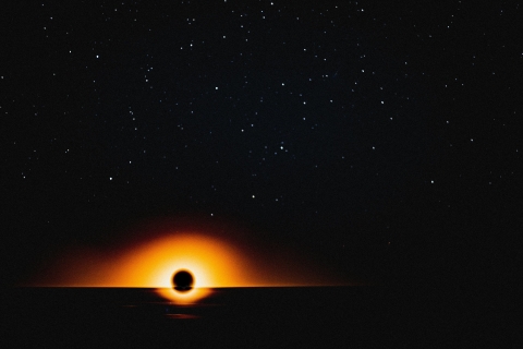 Image showing a black hole in space with mainly black background and the hole showing with a glowing ring of yellow, orange and red colour tones