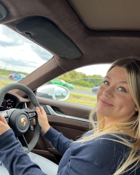 Daisy seated behind the wheel of a Porsche on test track