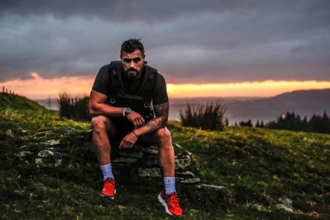 Josh Llewellyn-Jones in running clothes sitting on a mountain