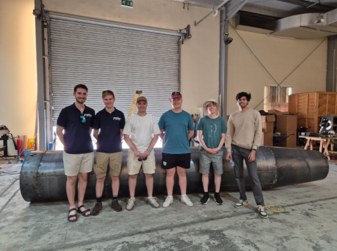 Students next to a mock-up of the rocket in the factory