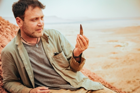 Dr Nizar Ibrahim in the Sahara desert holding a dinosaur tooth