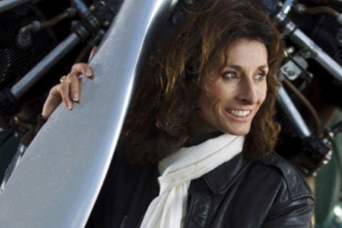 Tracey Curtis Taylor in leather jacket and scarf leaning against plane