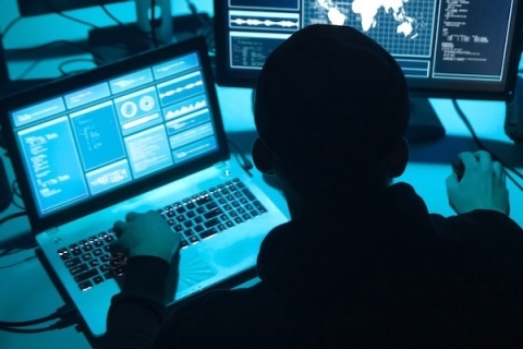 a hacker in the dark looking at computer screens