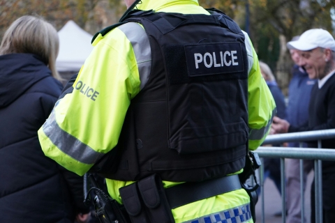 Image of the back of a policeman in a crowd wearing fluorescent jacket and bullet proof vest