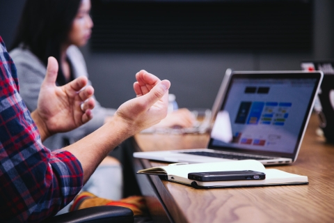A laptop on a table and a person's hands gesticulating