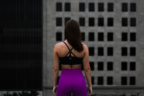 woman with her back to camera, wearing sports bra and purple leggings
