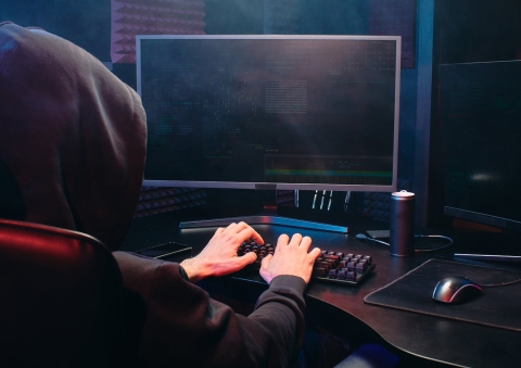 Person with a black hood up typing on a computer