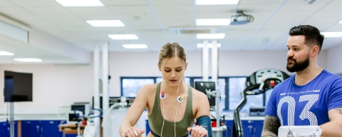 Student on bike machine with a trainer and hooked up to monitors