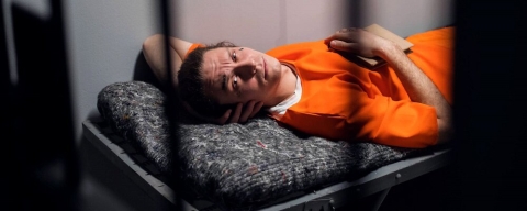 A prisoner in a cell in an orange jumpsuit