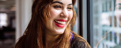 A postgraduate student standing at a window and smiling