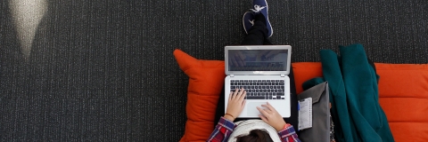 Aerial view of a person sitting on an orange sofa using a laptop