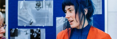 A person talking whilst stood in front of a poster board