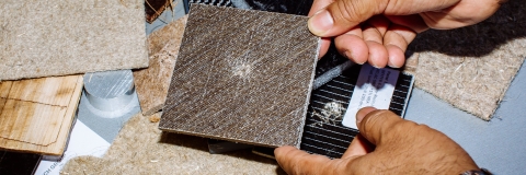 male hands hold small solid square panel which is made from materials including plant waste