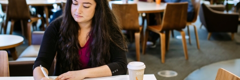 Student taking notes in university library cafe