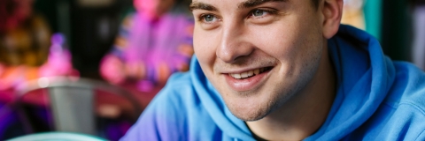 A male student smiling whilst wearing a blue hoodie
