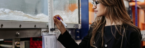 Student measures temperature of container, taking notes in notebook at Technology Facilities