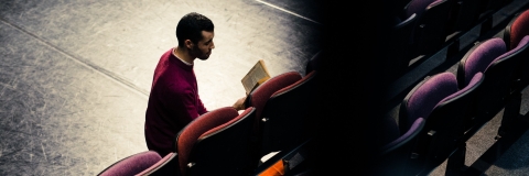 Man reading a play in dimly-lit theatre space