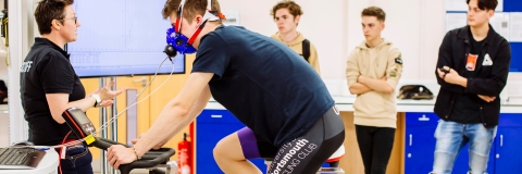 Male student training on stationary bike in front of class