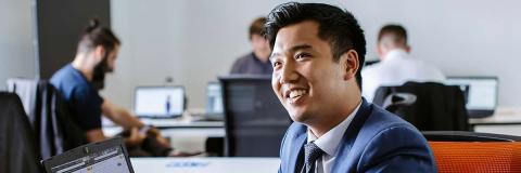 Smiling man in suit seated with laptop open