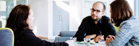 Male staff member facing two female staff members in meeting